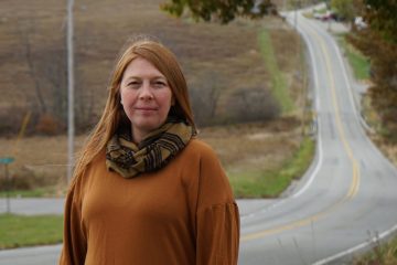 A woman stands on a country road.