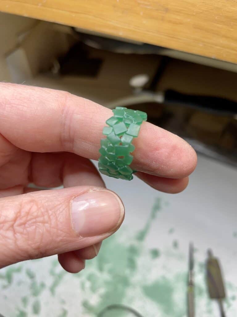 Carved wax ring composed of cubes, being shown on index finger.