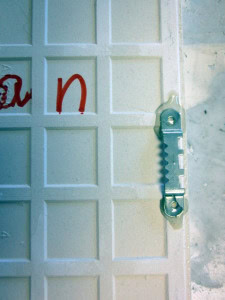 Close-up of a metal latch attached to a white, grid-patterned surface with red scribbles on the left side.