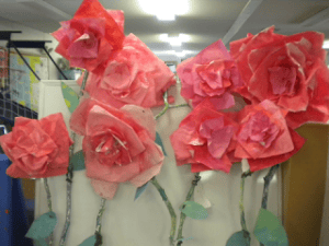 Large pink and red paper roses showcased in a room with fluorescent lighting.