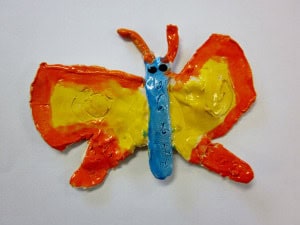 A colorful clay butterfly with yellow wings outlined in orange and a blue body, set against a white background.