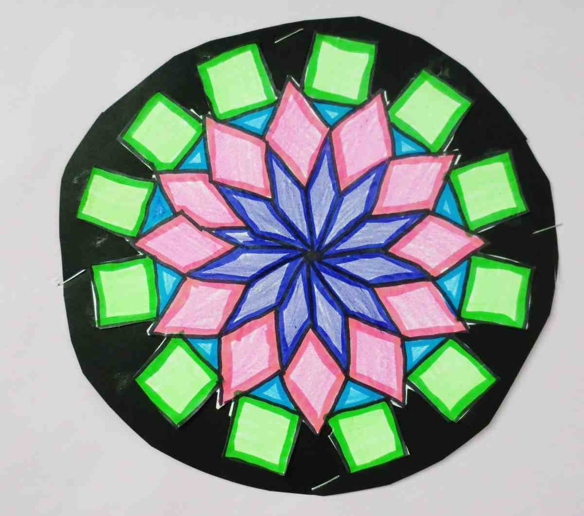 A colorful Pattern Block Picture mandala featuring blue, pink, and green shapes on a black circular background.