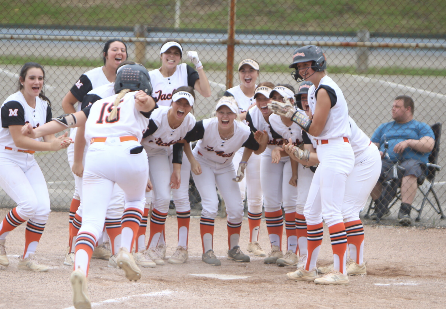 A softball player is greeted at home after hitting a home run