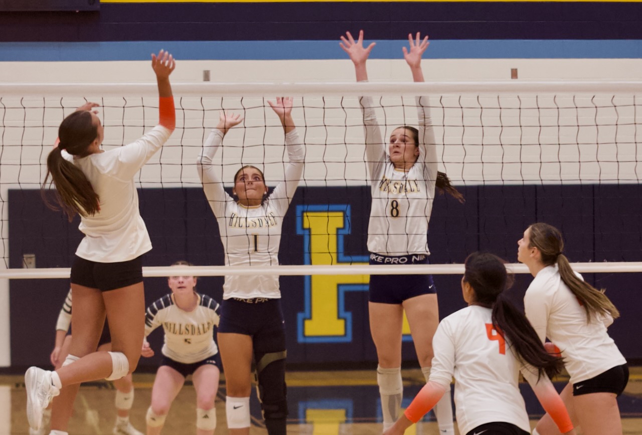 two volleyball players team up to block a shot