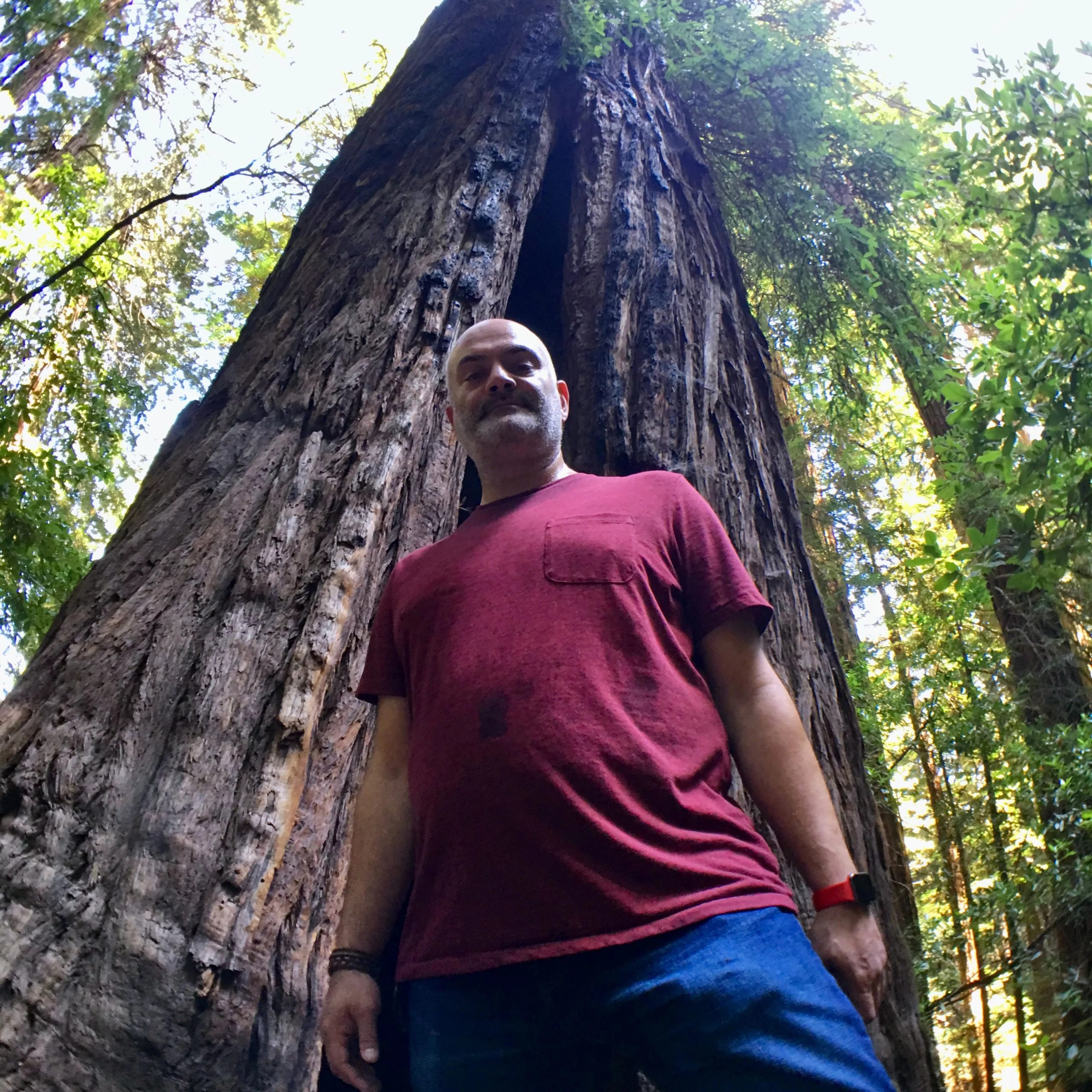 Mazi in front of a large tree. weraing a red shirt and blue jeans