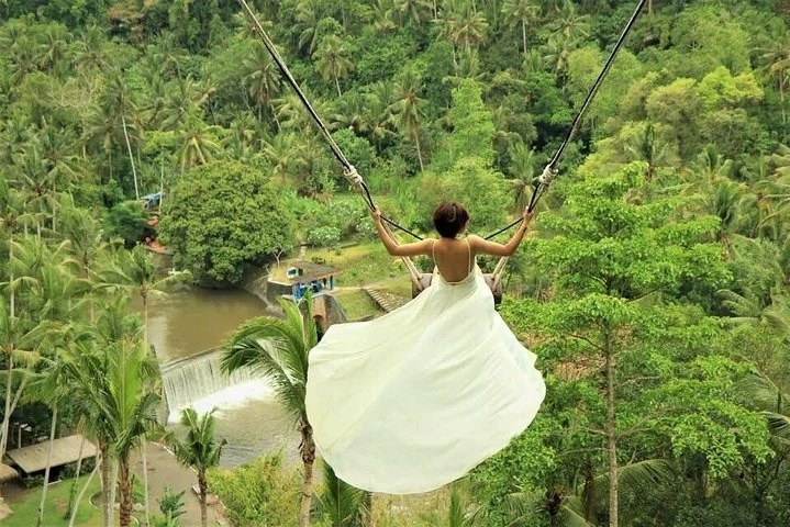 A woman swings high above the lush tropical jungle in Bali, showcasing the vibrant scenery and adventure.