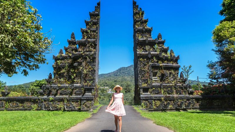 A female tourist takes a photo in front of a traditional Balinese gate. The cultural design creates a unique background.