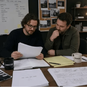 A film director and producer collaborating at a desk with scripts and storyboards during the pre-production workflow phase.