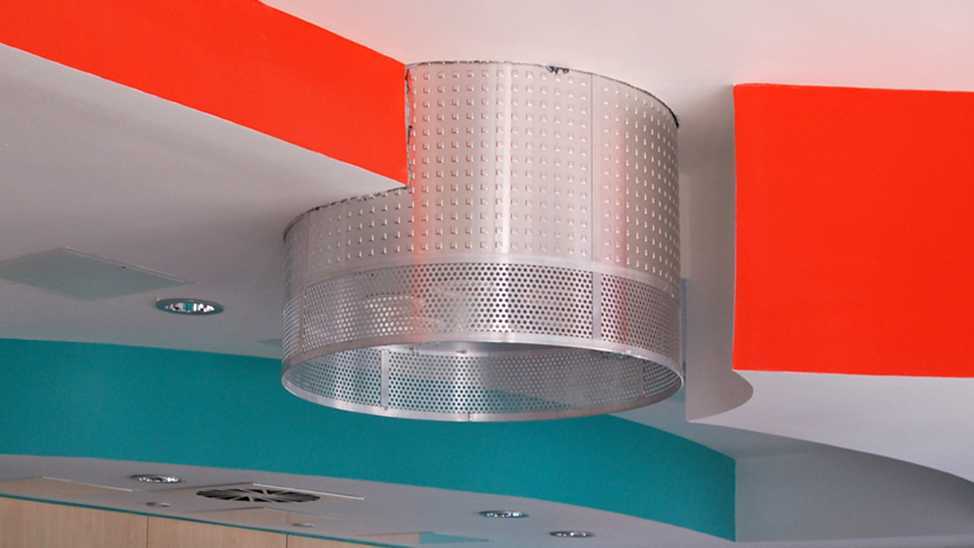 Circular suspended lighting feature in the Teenage Cancer Care unit, set against red and turquoise ceiling details.