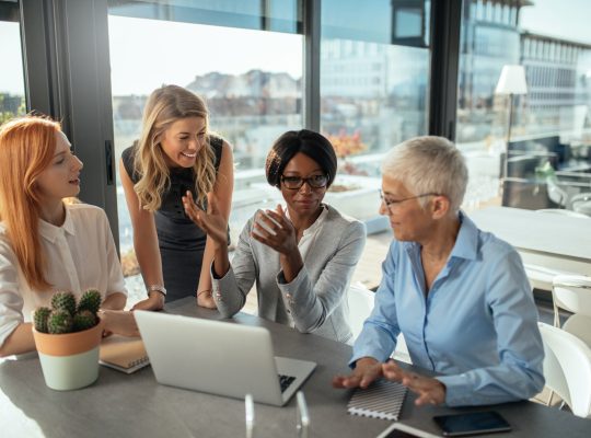 Group of diverse female business owners smiling and working together around a laptop