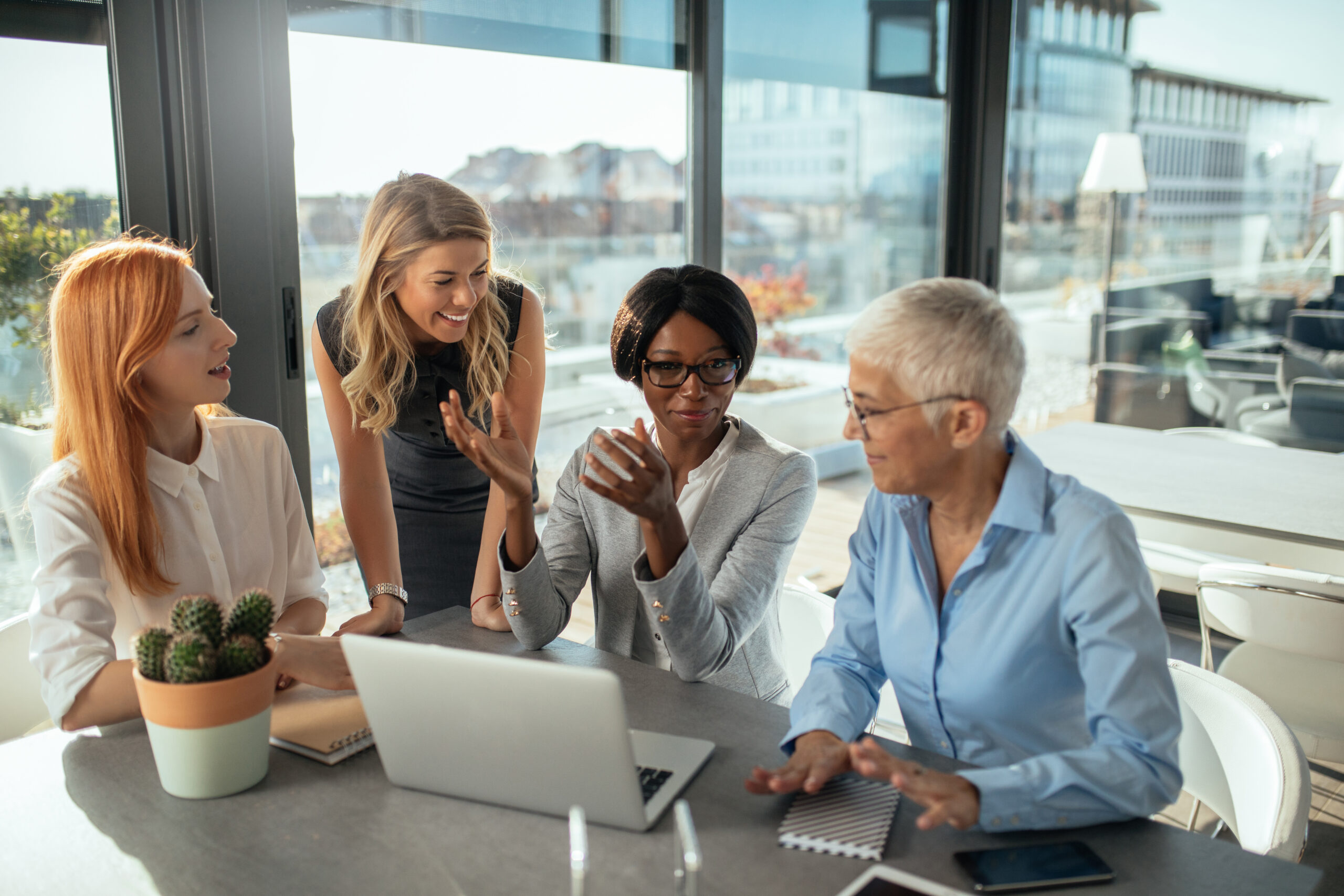 Group of diverse female business owners smiling and working together around a laptop