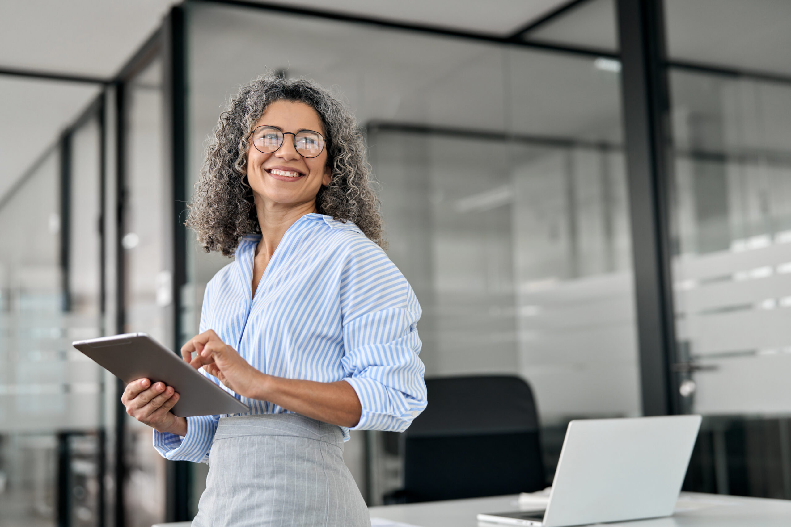 Smiling female CEO holding an iPad in a modern office setting, representing empowered empathetic leadership.