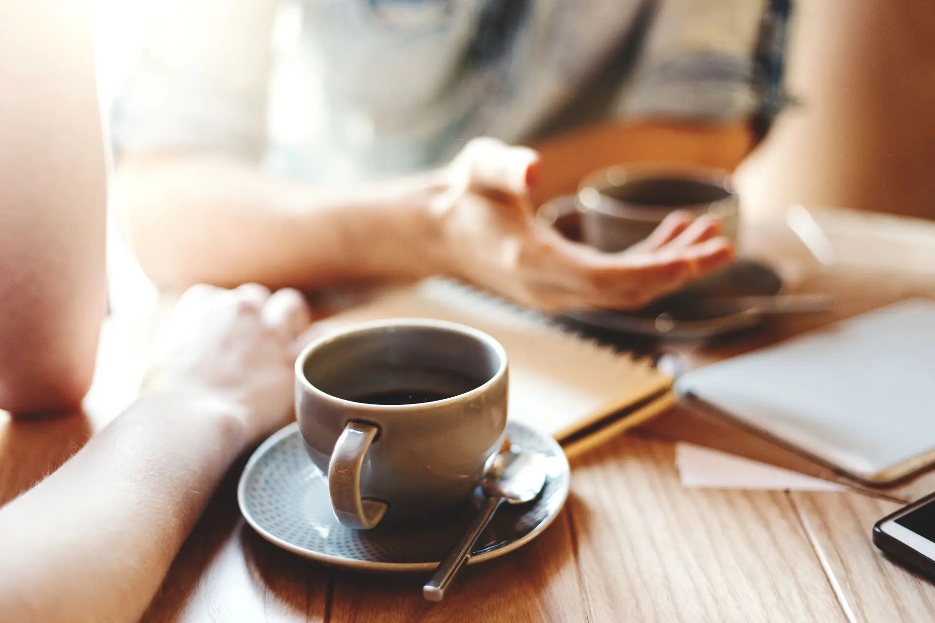Two people having a coffee meeting with a journal and tablet on the table, symbolizing open conversation and professional connection.