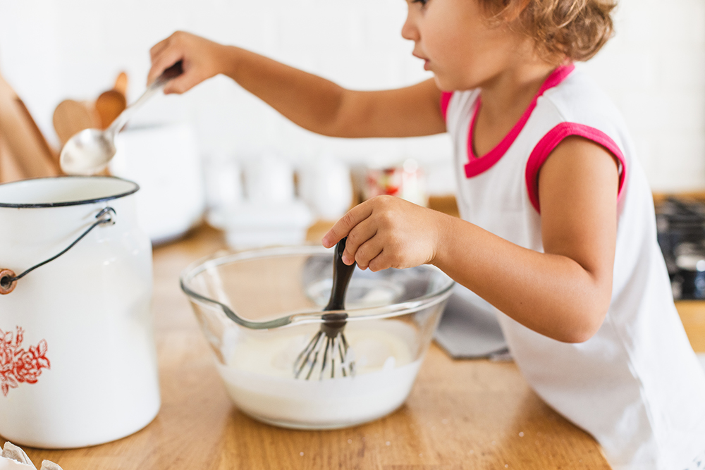 3 years cute girl preparing dough for pancakes at the kitchen.