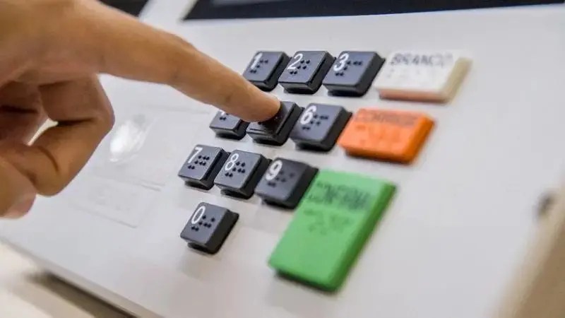 Mão pressionando o teclado de uma urna eletrônica para registrar um voto.