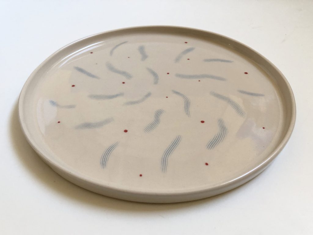 Hand thrown plate with blue wave inlay and small red dots glazed in tranparent glaze. It is warm off white colour.