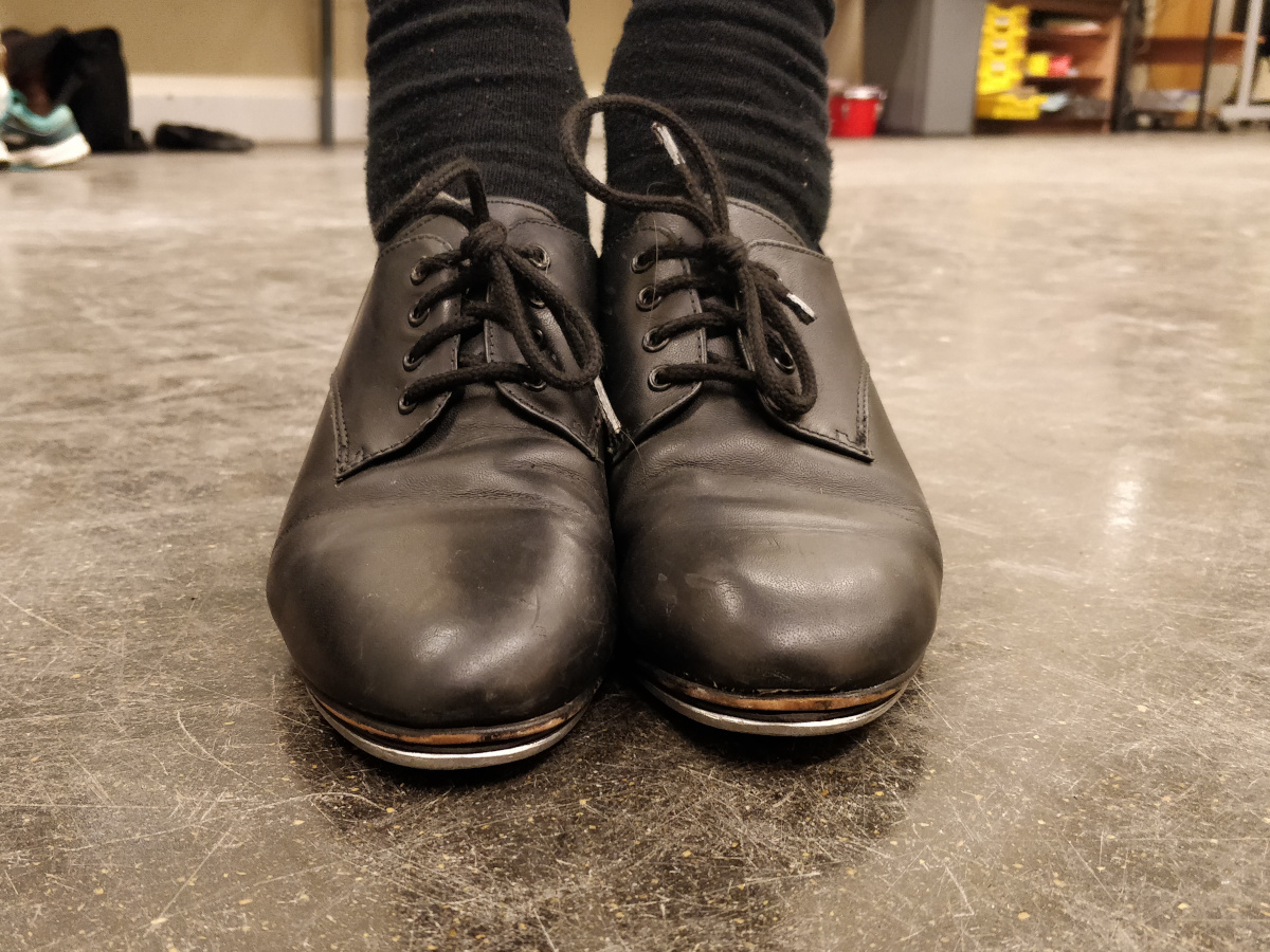 Close up of a pair of black tap dancing shoes on a dance floor studio.