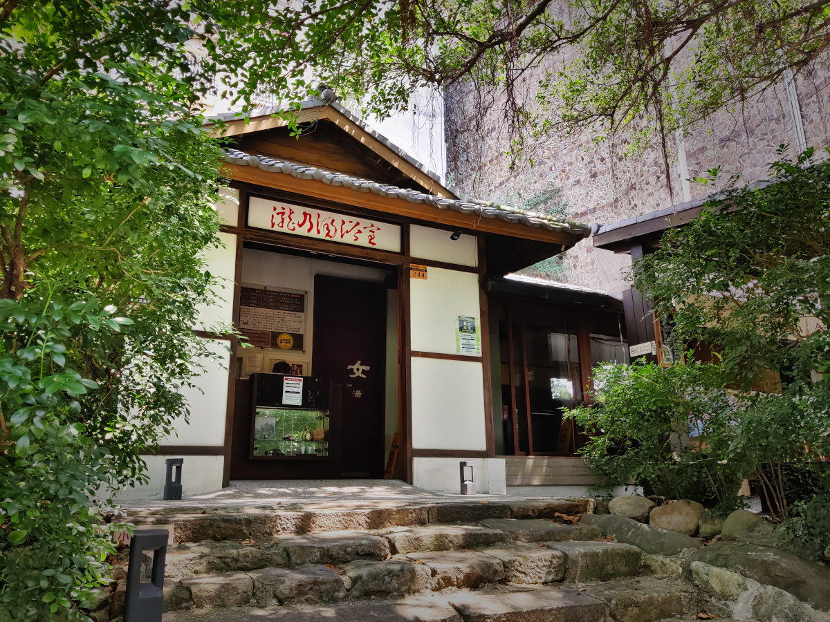 Exterior of a steps leading to a black and white building in a leafy area. It is a bath house for the hot springs in Taiwan