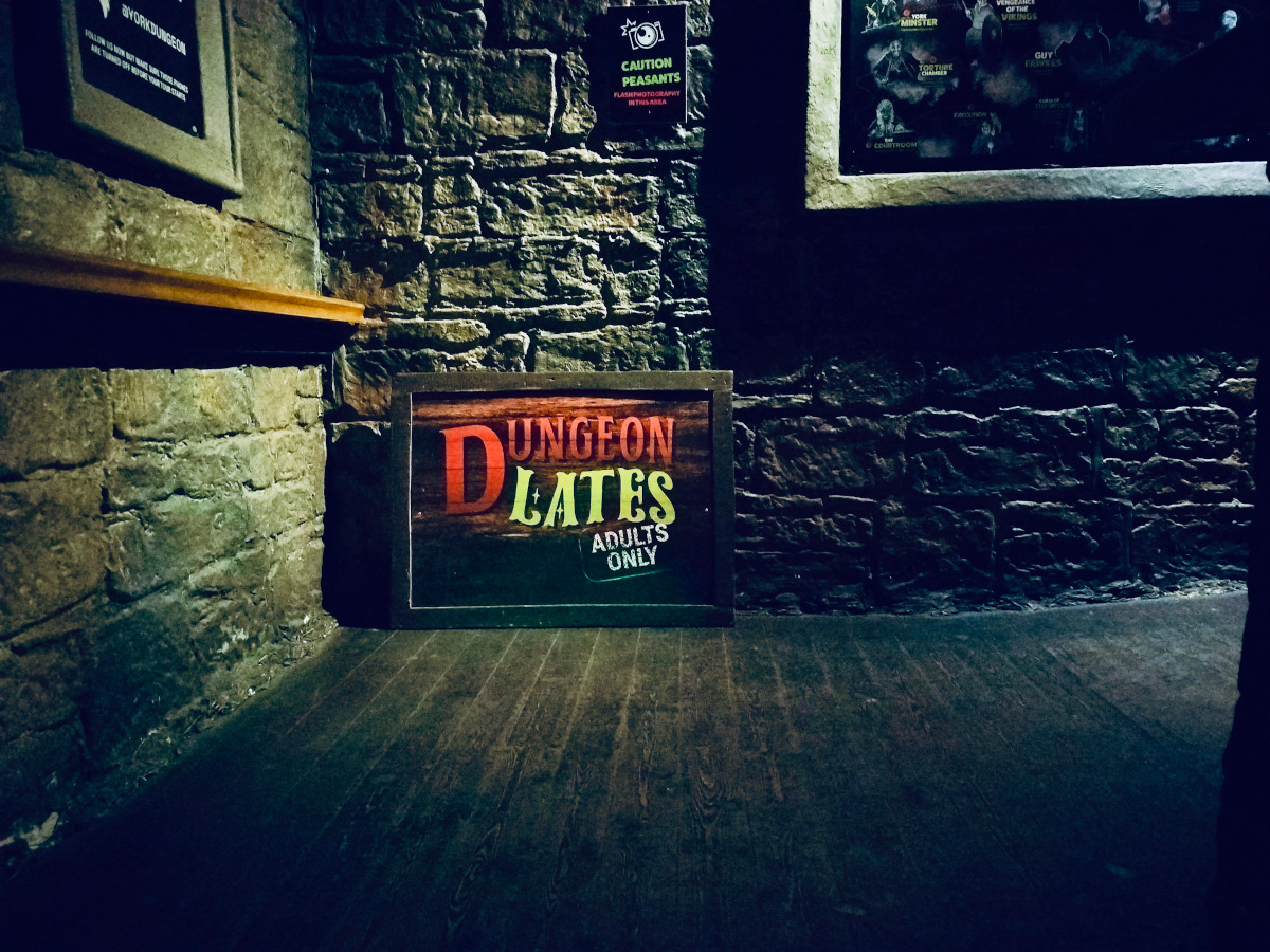 A sign on the floor of an old brick room. It reads 'Dungeon Lates, Adults Only'. You will see this when you experience York Dungeon lates