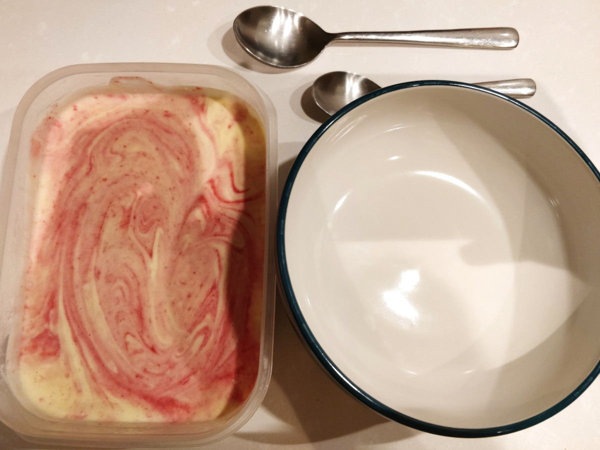 Looking down at an empty bow, two spoons, and a tub full of the delicious looking results of making ice cream from scratch