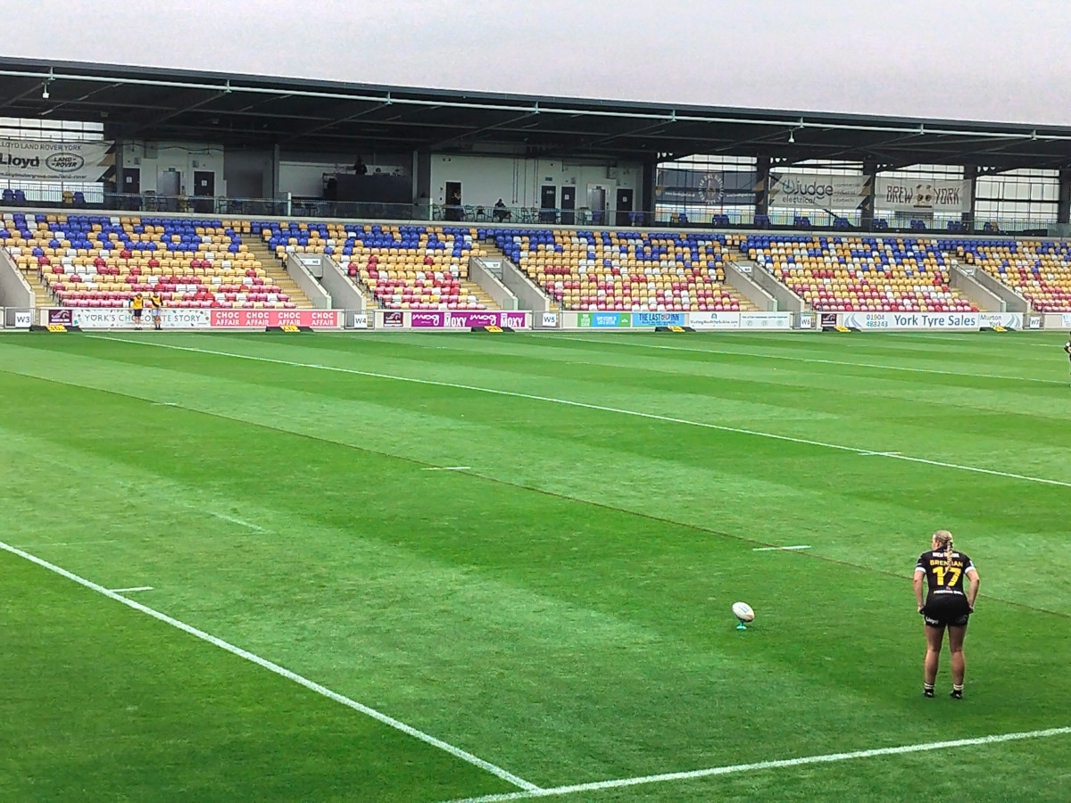 A female rugby player on the pitch ready to take a kick in a stadium.