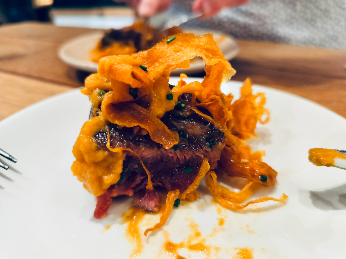 Close up of a plate which has a piece of sirloin steak topped with pumpkin crisps. This is a dish called Solomillo and can be tried on a Pintxos Tour In San Sebastián