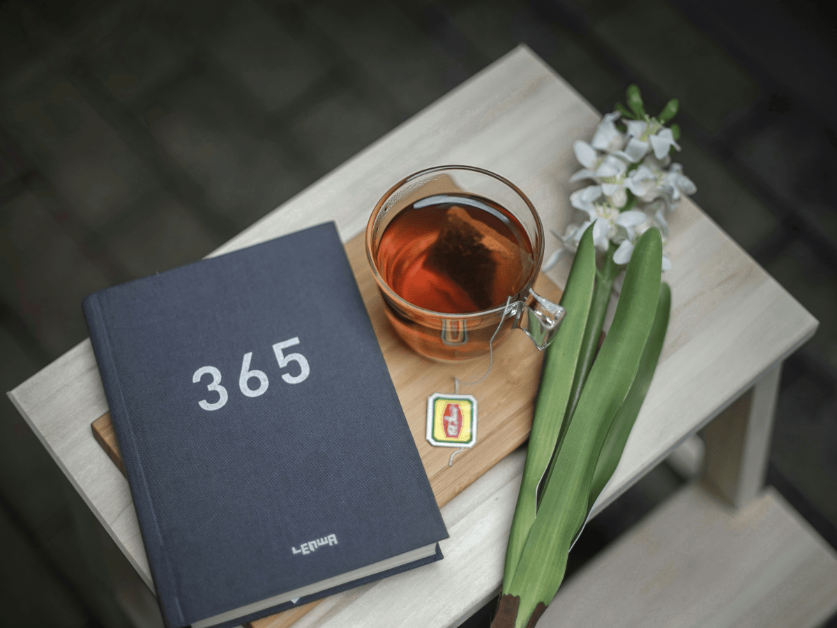 A notepad which says 365 on it, it's next to a nice cup of tea and a freshly picked flower