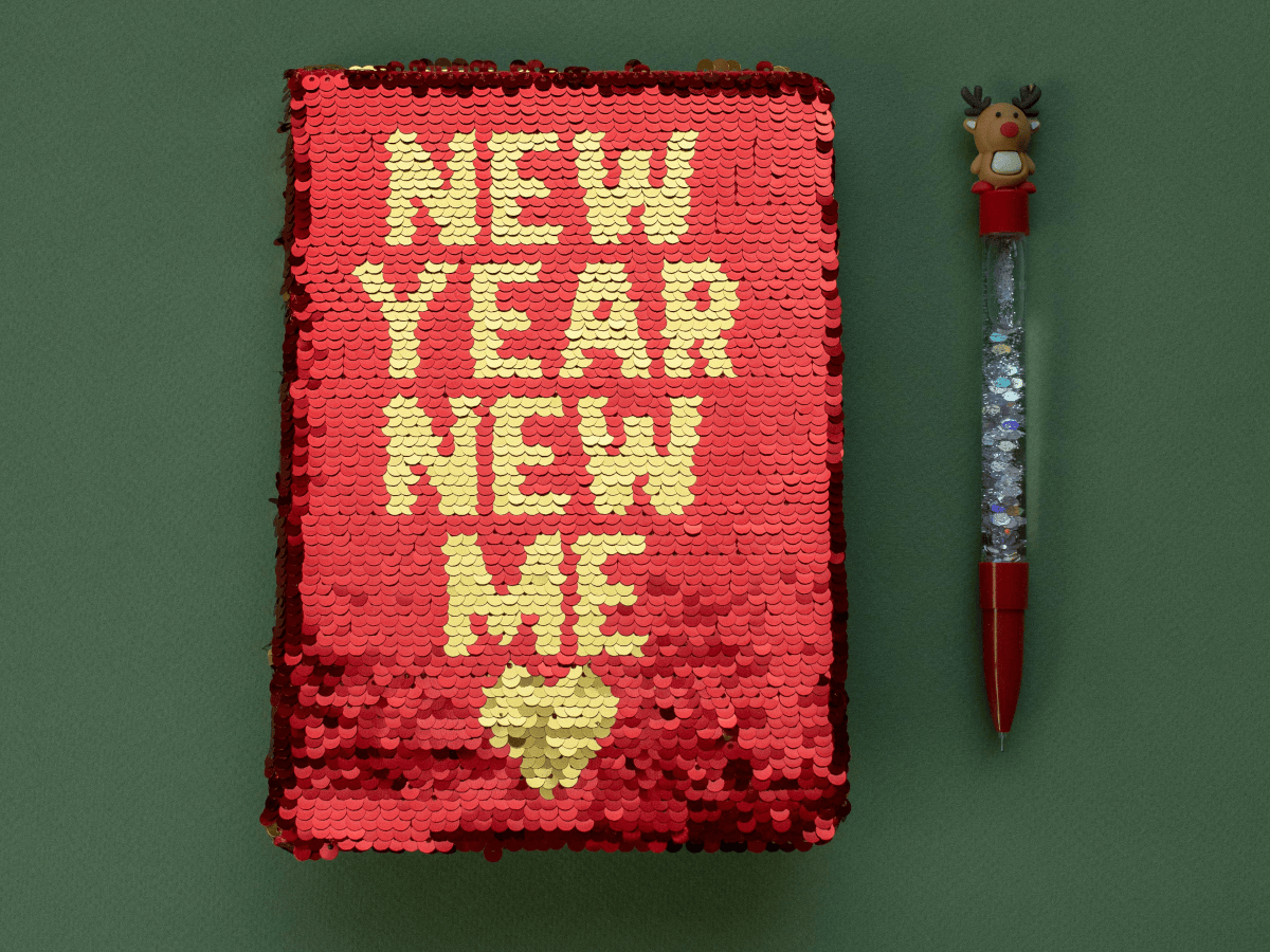 A sparkly red book on a green background. There is gold text on the front of the book which reads 'new year new me'