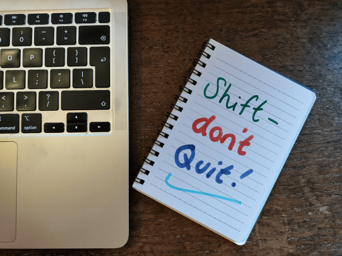 A note pad next to a laptop keyboard. The notepad reads 'shift- don't quit' and is a tip on how to set a new year's resolution you'll actually want to keep