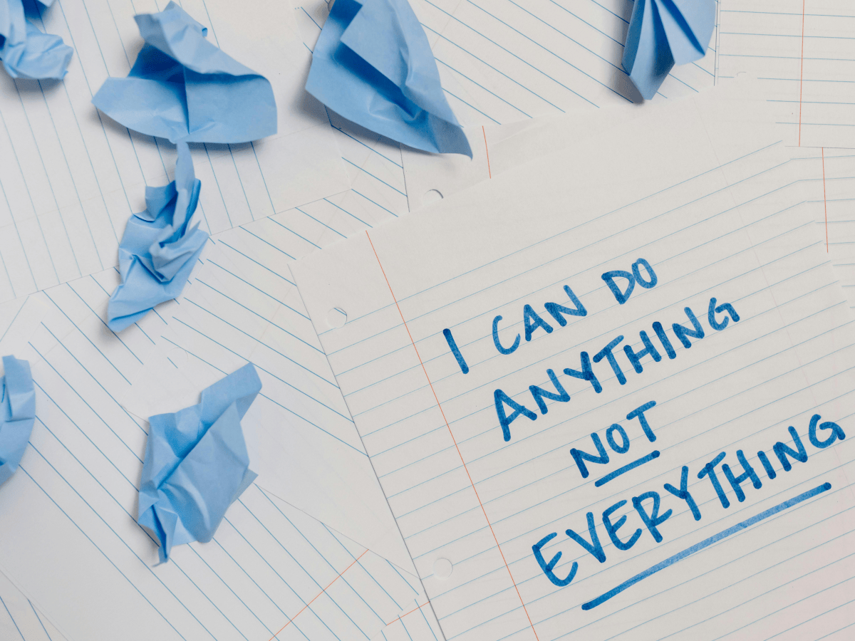 A piece of paper with blue writing on which reads 'I can do anything, NOT everything' and there are scrumpled up pieces of blue paper dotted around. A helpful tip in how to set a new year's resolution you'll actually want to keep