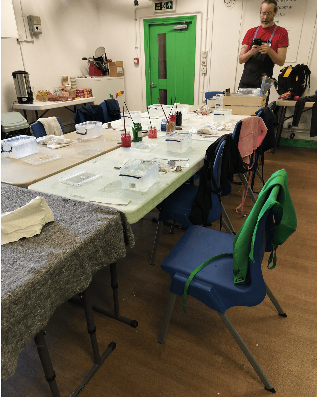 Looking into a room which is laid out for a bauble marbling workshop. There are paints on the tables, and chairs around the edges. It looks a crafty environment.