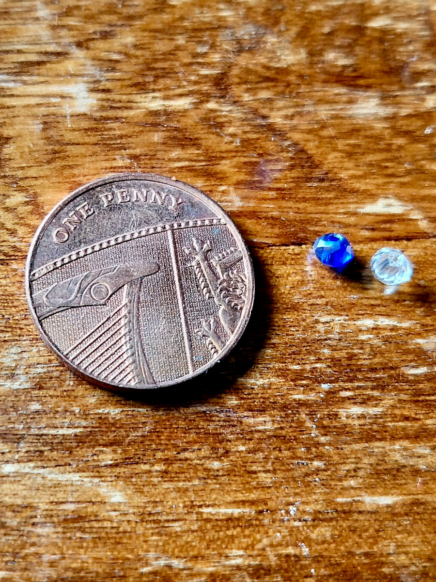 A one penny coin next to a blue and clear bead, to demonstrate how small the beads were in the wire beading kit.