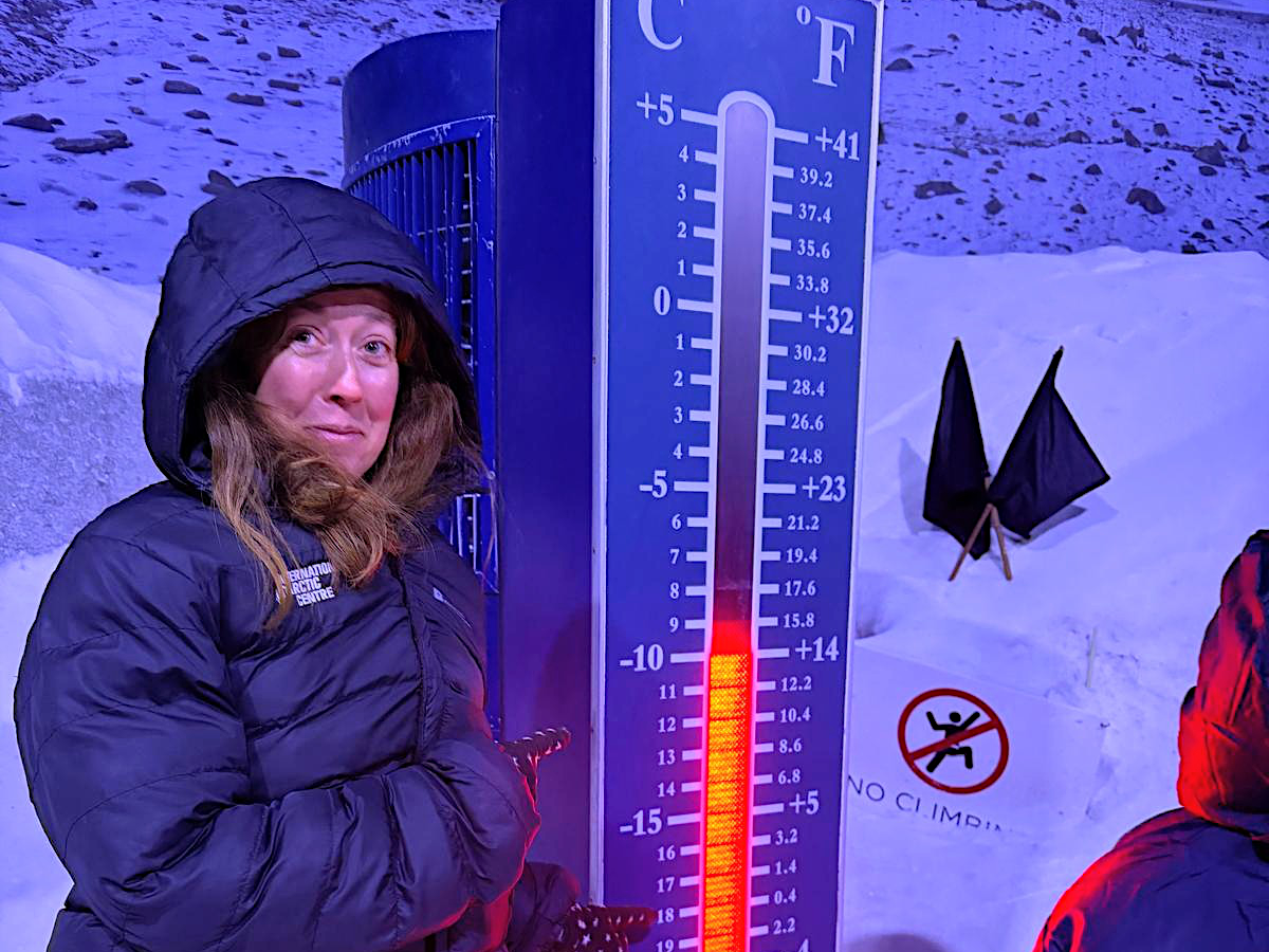 Challenge Fifty-Two, a white woman wrapped up in a thick puffer jacket and pointing at a thermometer showing a cold temperature