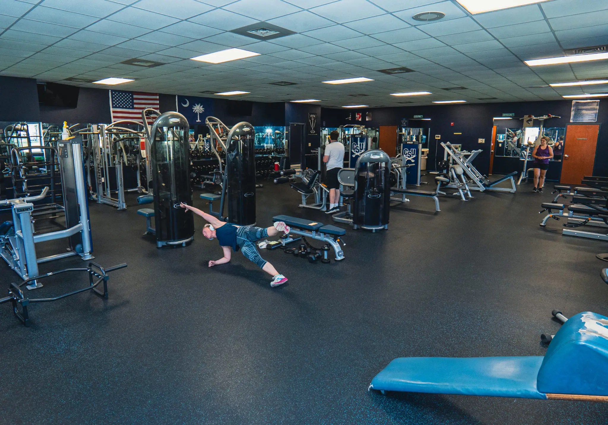 People working out at the gym. The weight room has multiple machines and weights