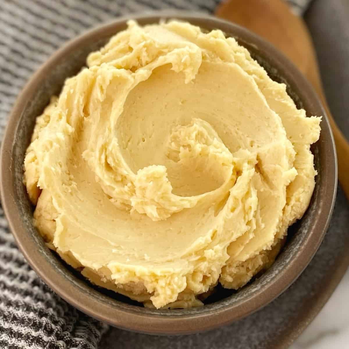 yellow coloured butter in a small grey bowl with a small wooden spoon on the side.