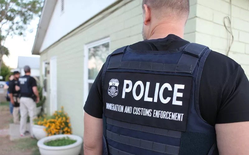 An ICE officer outside a house