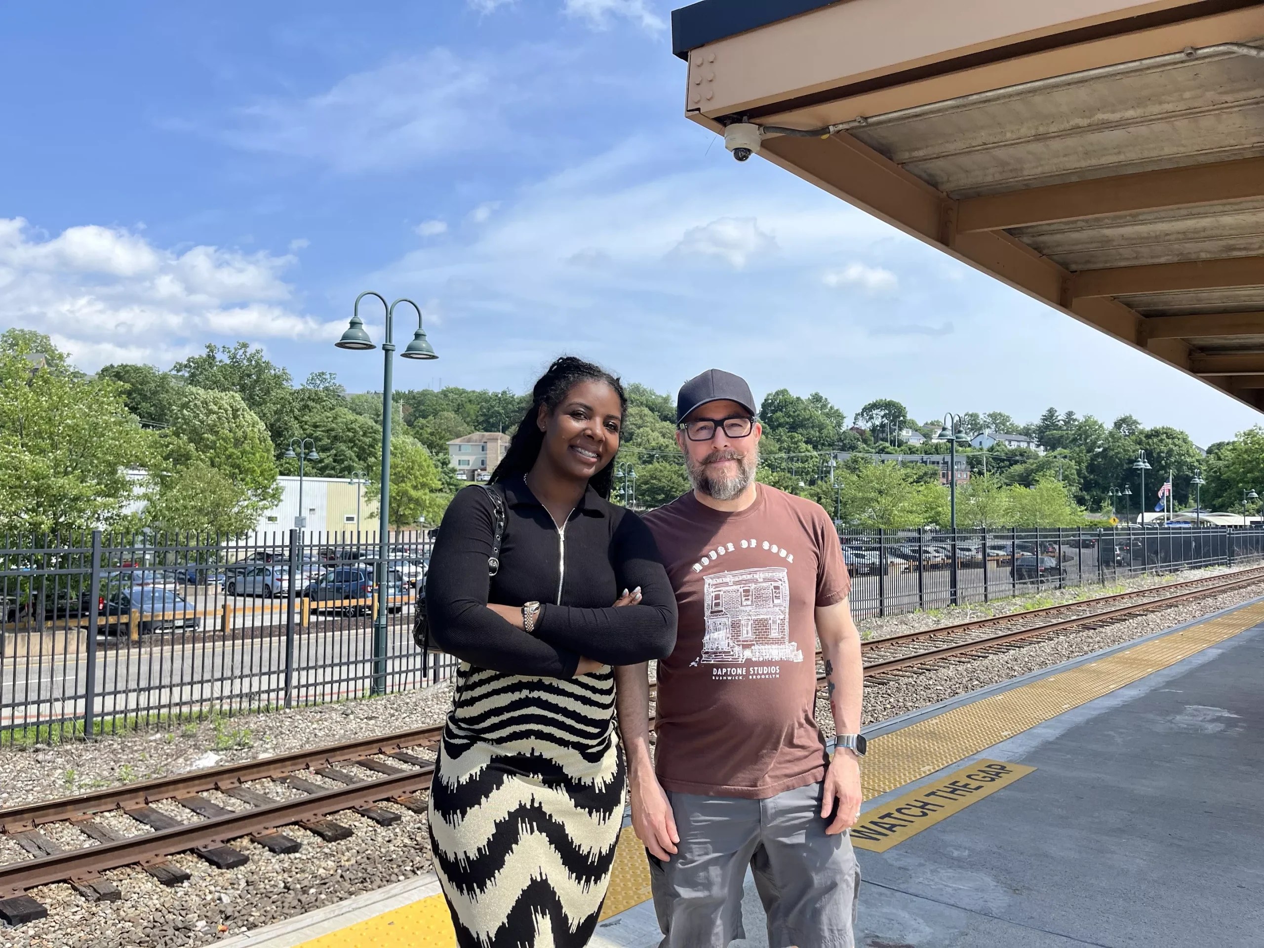 A photo of a man and woman smiling next to each other on a train station platform.