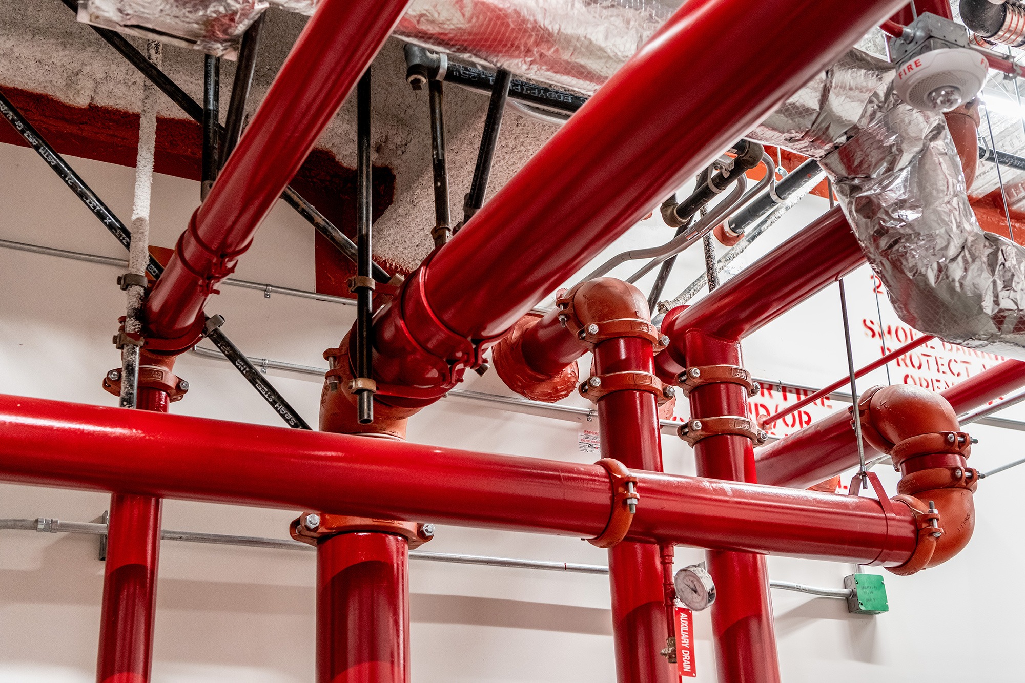 Red and silver pipes line the white walls of a fire protection engineering job site.