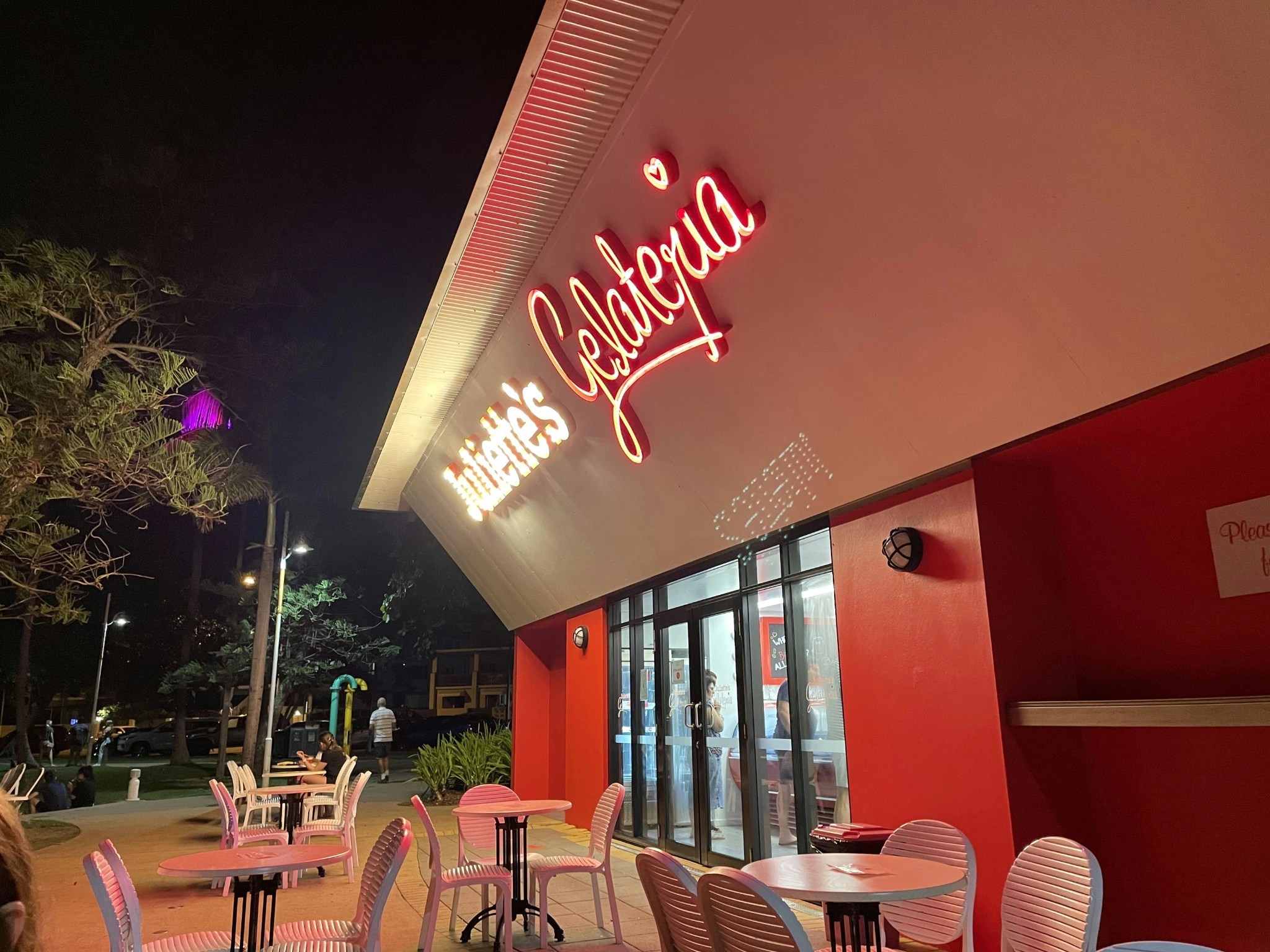 Neon-lit storefront of Juliette's Gelateria with pink outdoor seating under a starry night sky