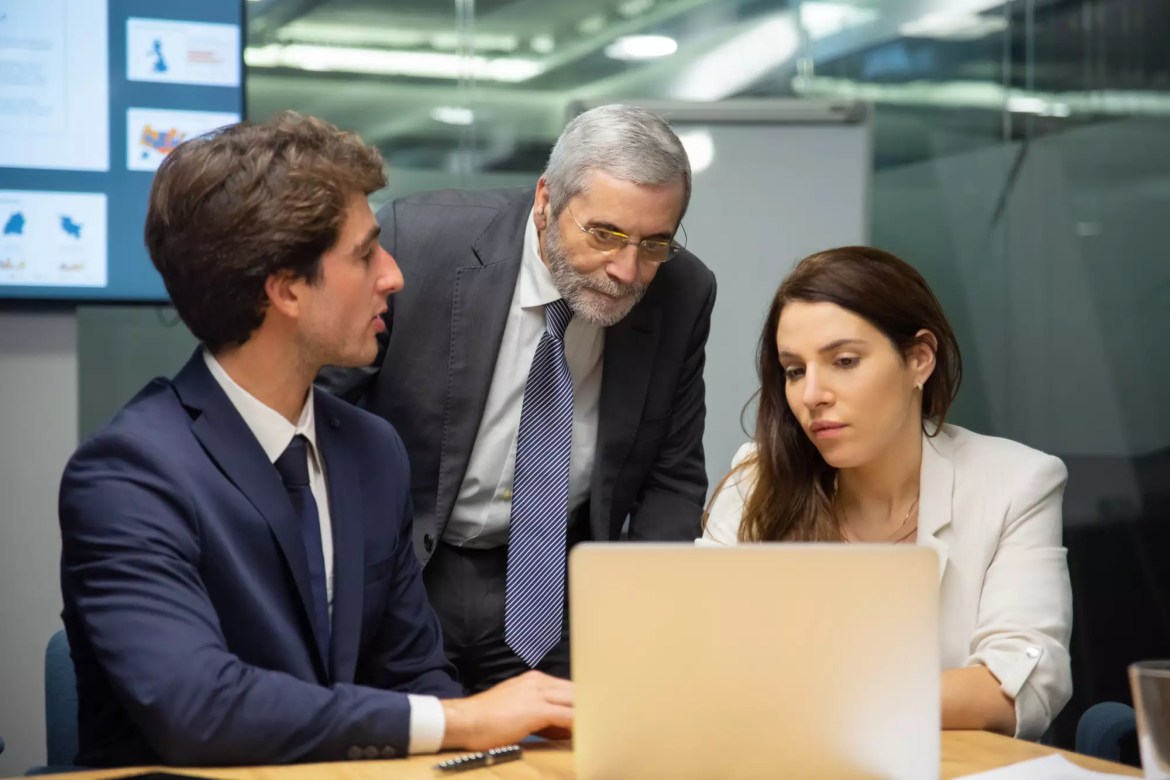 Business team collaborating around a laptop during a meeting in a modern office.