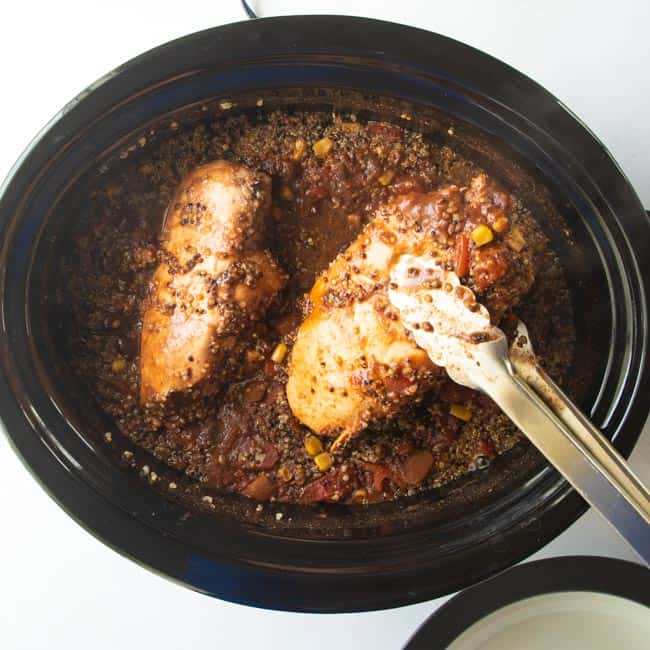 chicken breasts removed with tongs from a slow cooker