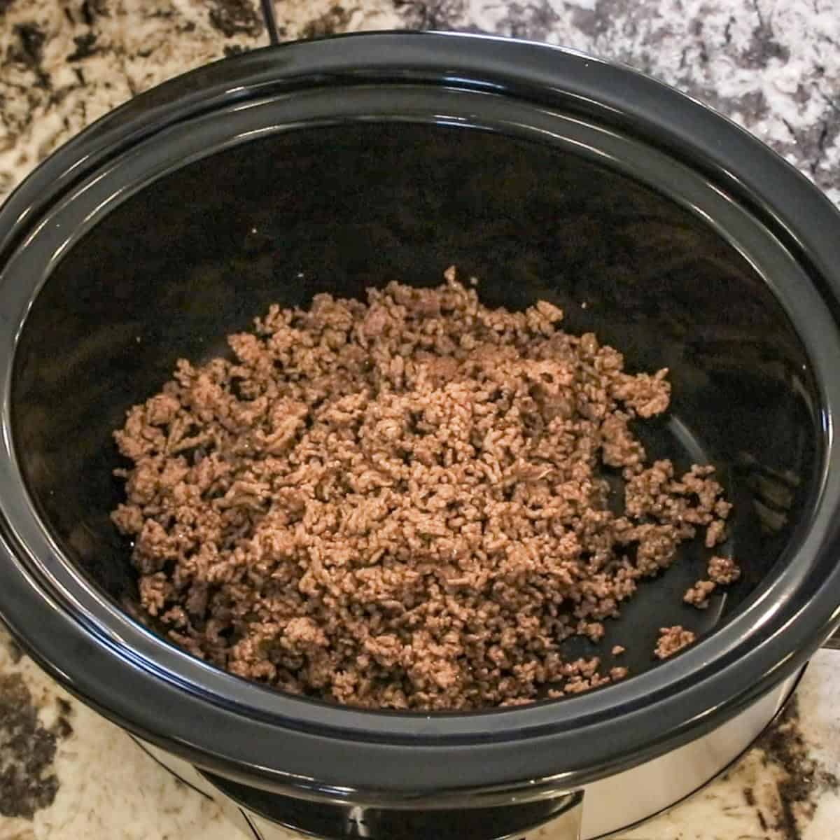 ground beef in the bottom of a black slow cooker