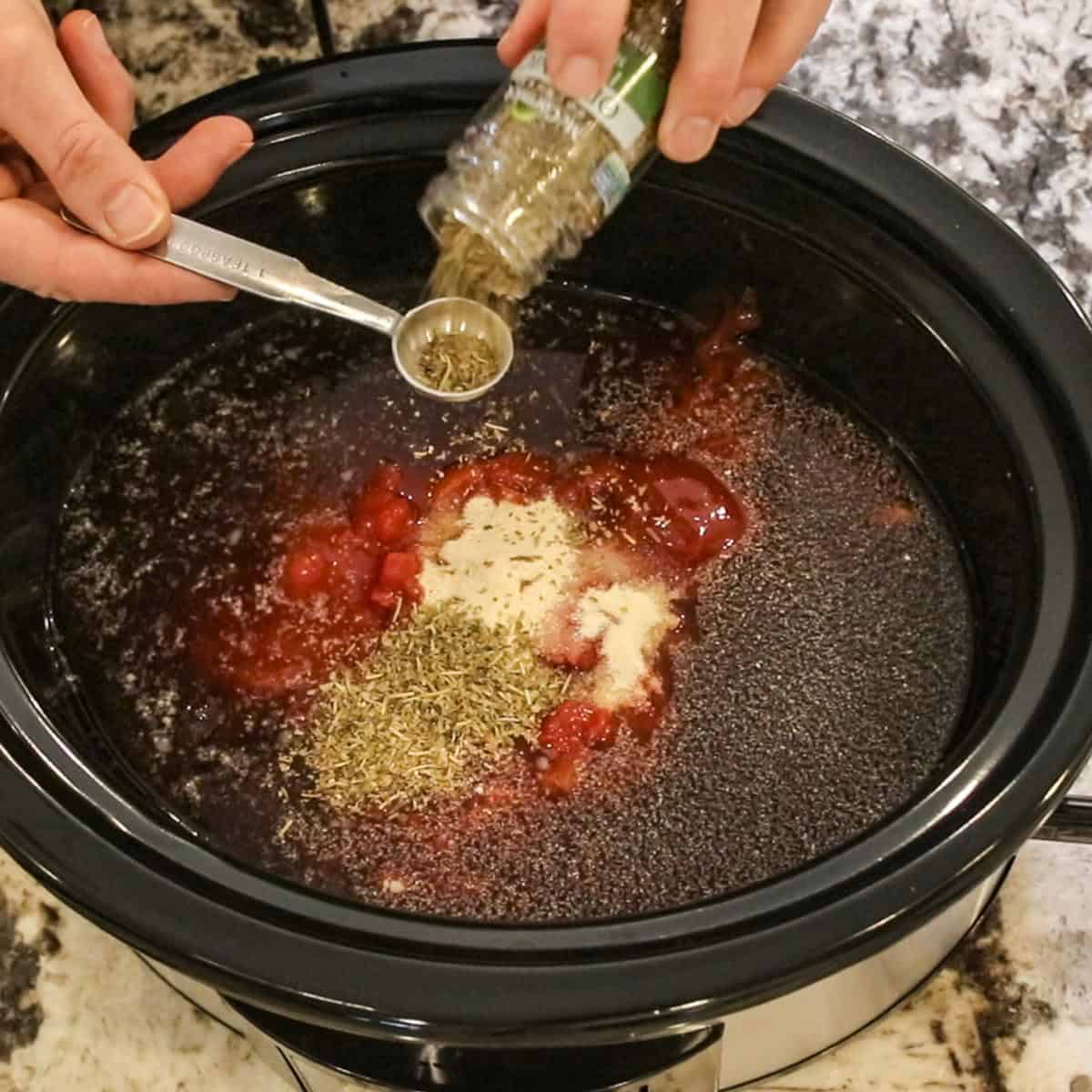 spices being added to a soup in a slow cooker