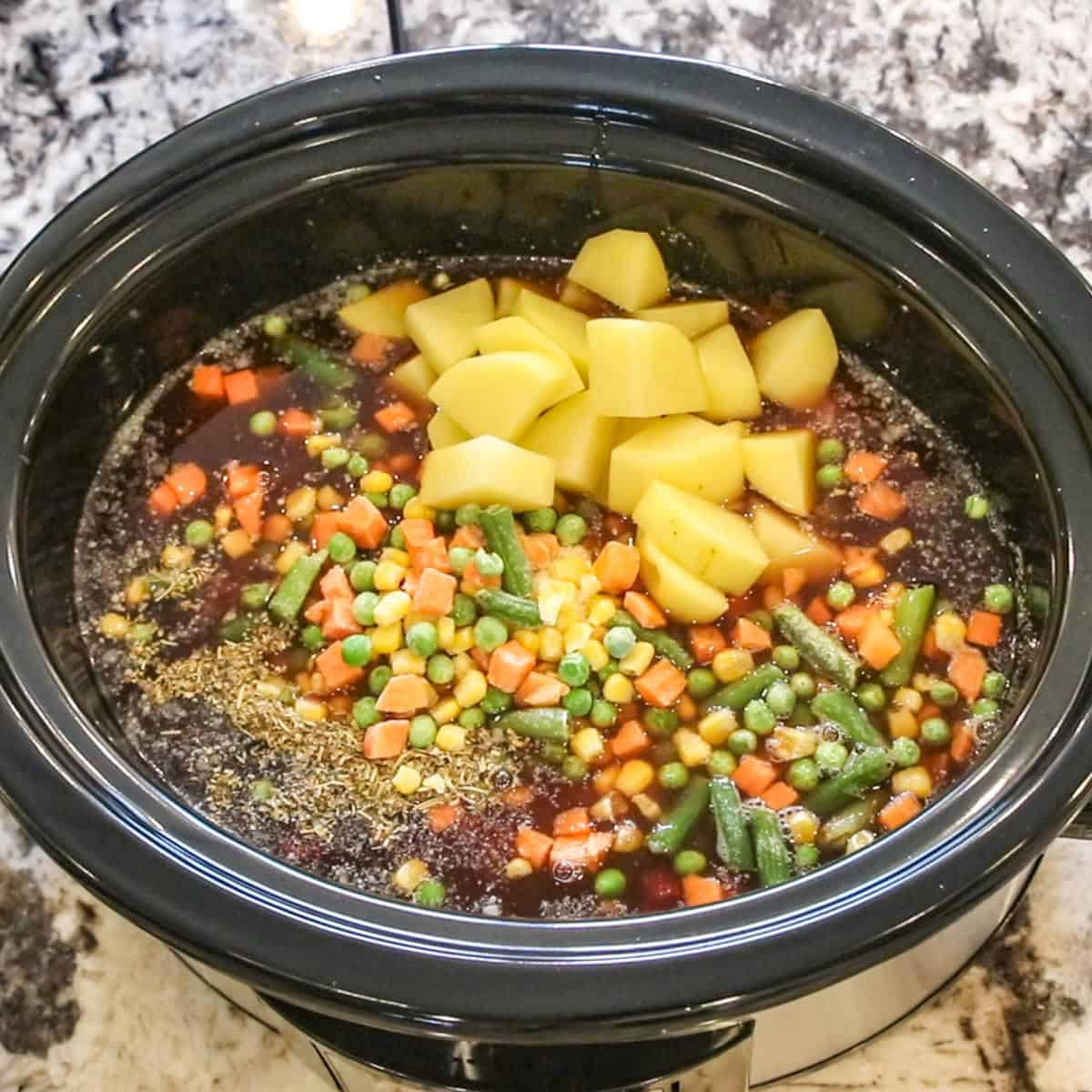 frozen mixed vegetables and diced potatoes added to a soup in a slow cooker