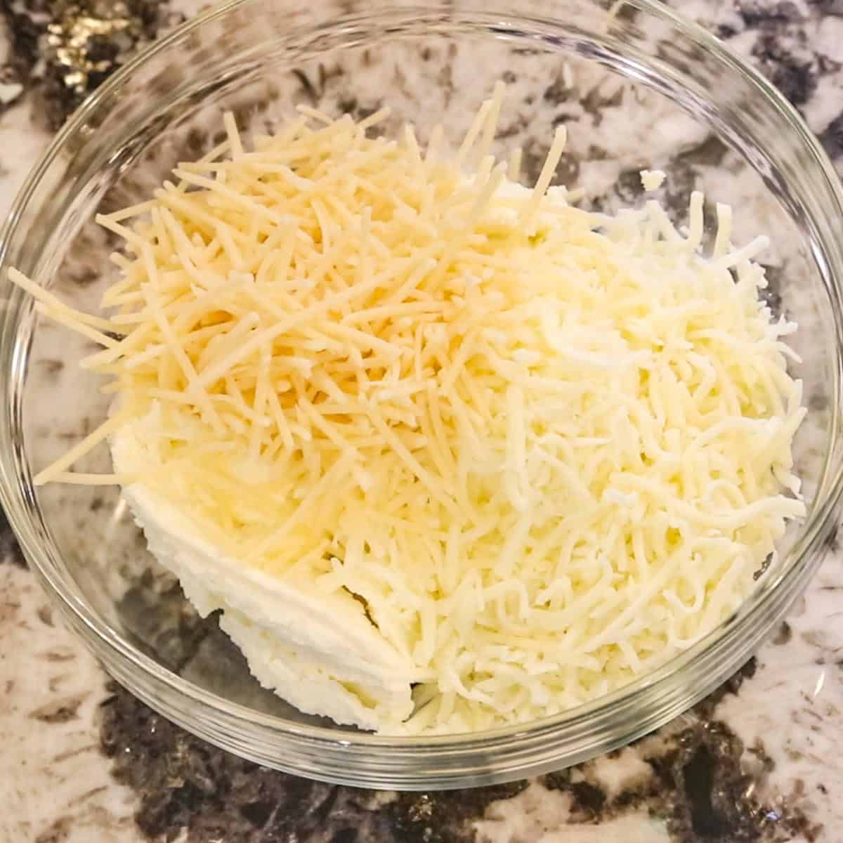 two shredded cheeses and ricotta cheese in a clear glass bowl