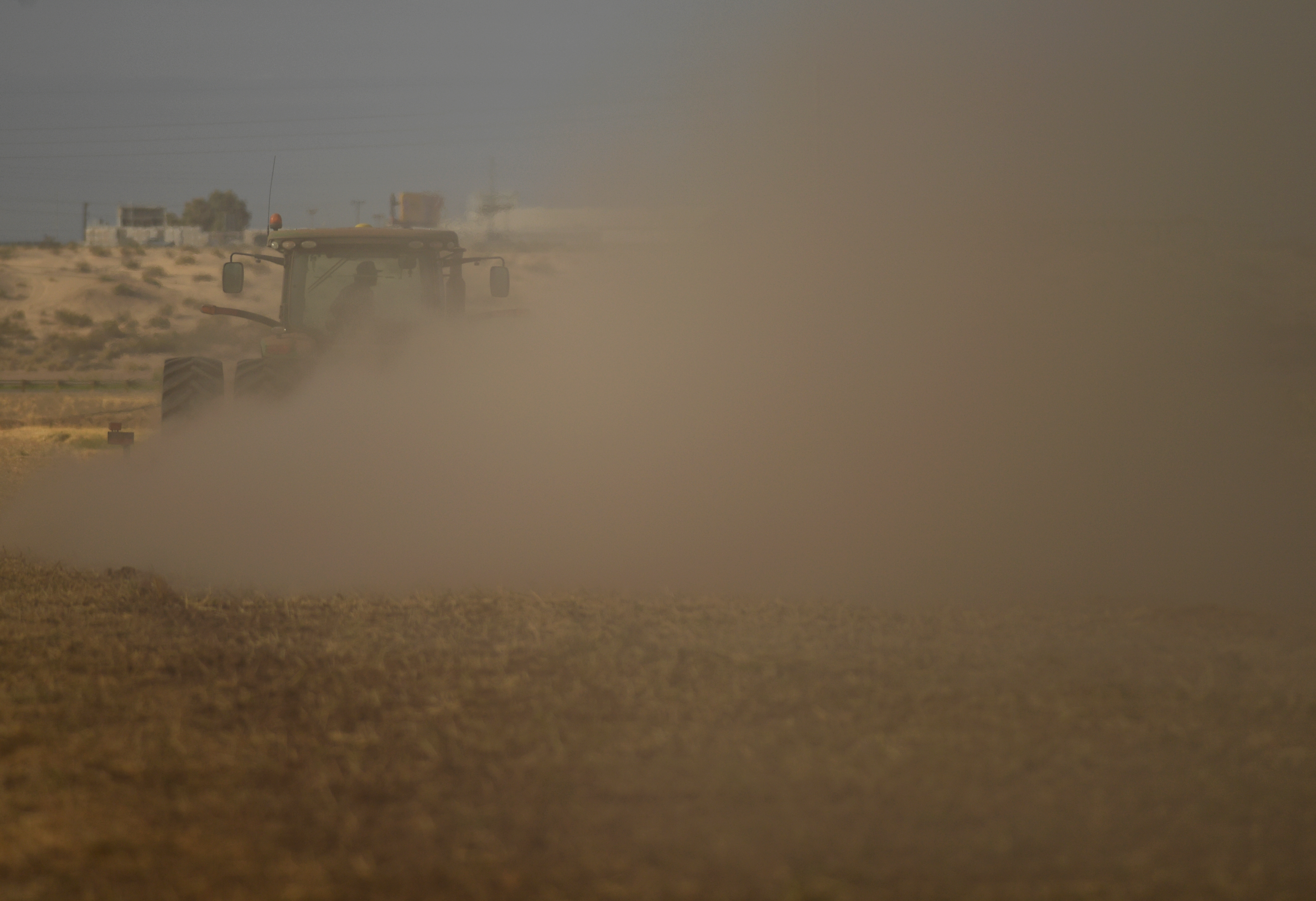 A farmer kicks up dust as ...