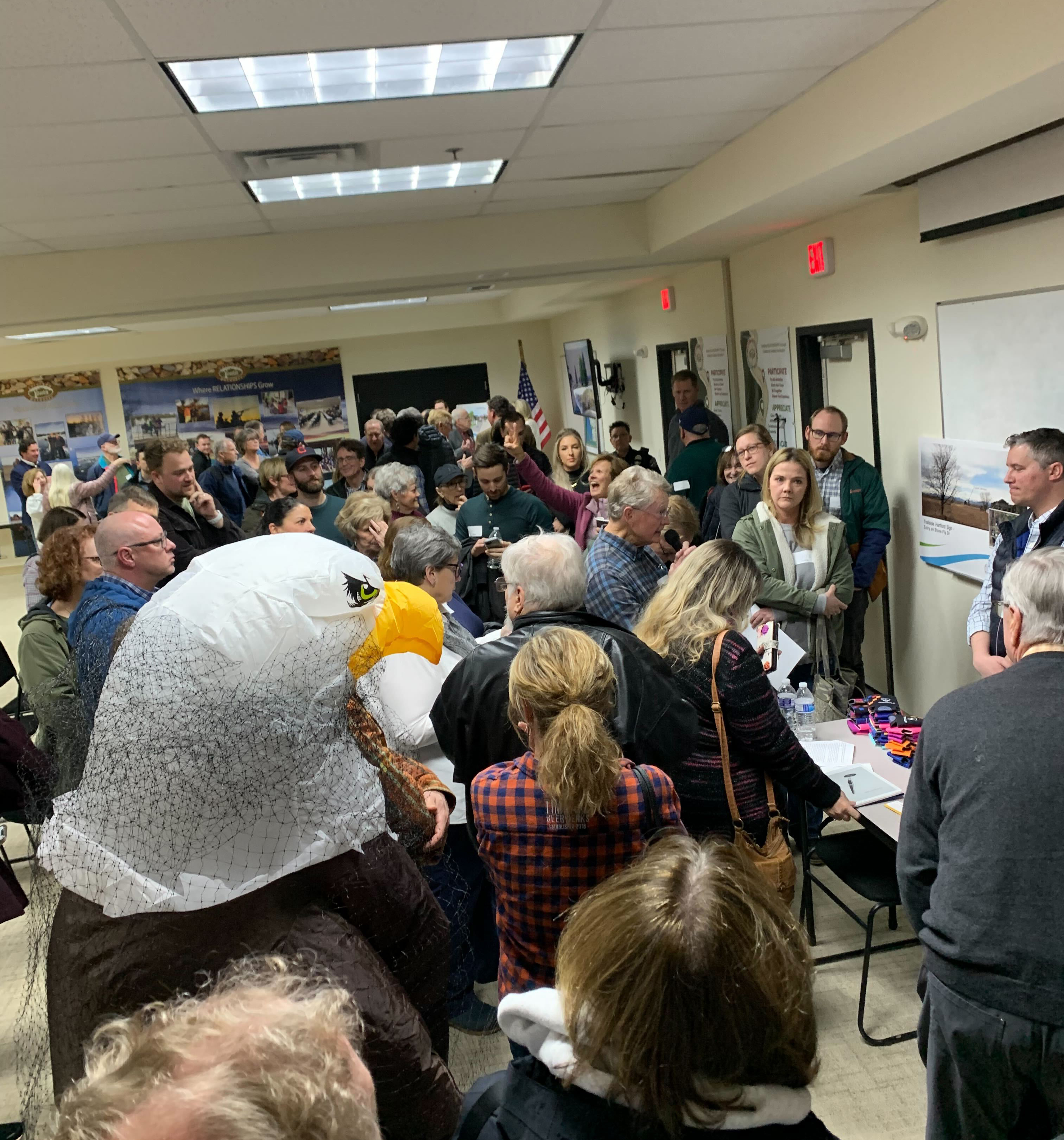 A man dressed as a bald eagle stands with a crowd in front of representatives of Topgolf during a public meeting in Timnath on Feb. 13, 2023. Residents in the fast-growing community near Fort Collins are trying to stop the company from building a facility in town, claiming Topgolf's trademark safety nets pose a risk to migratory birds in flight. (Photo by John Aguilar/The Denver Post)