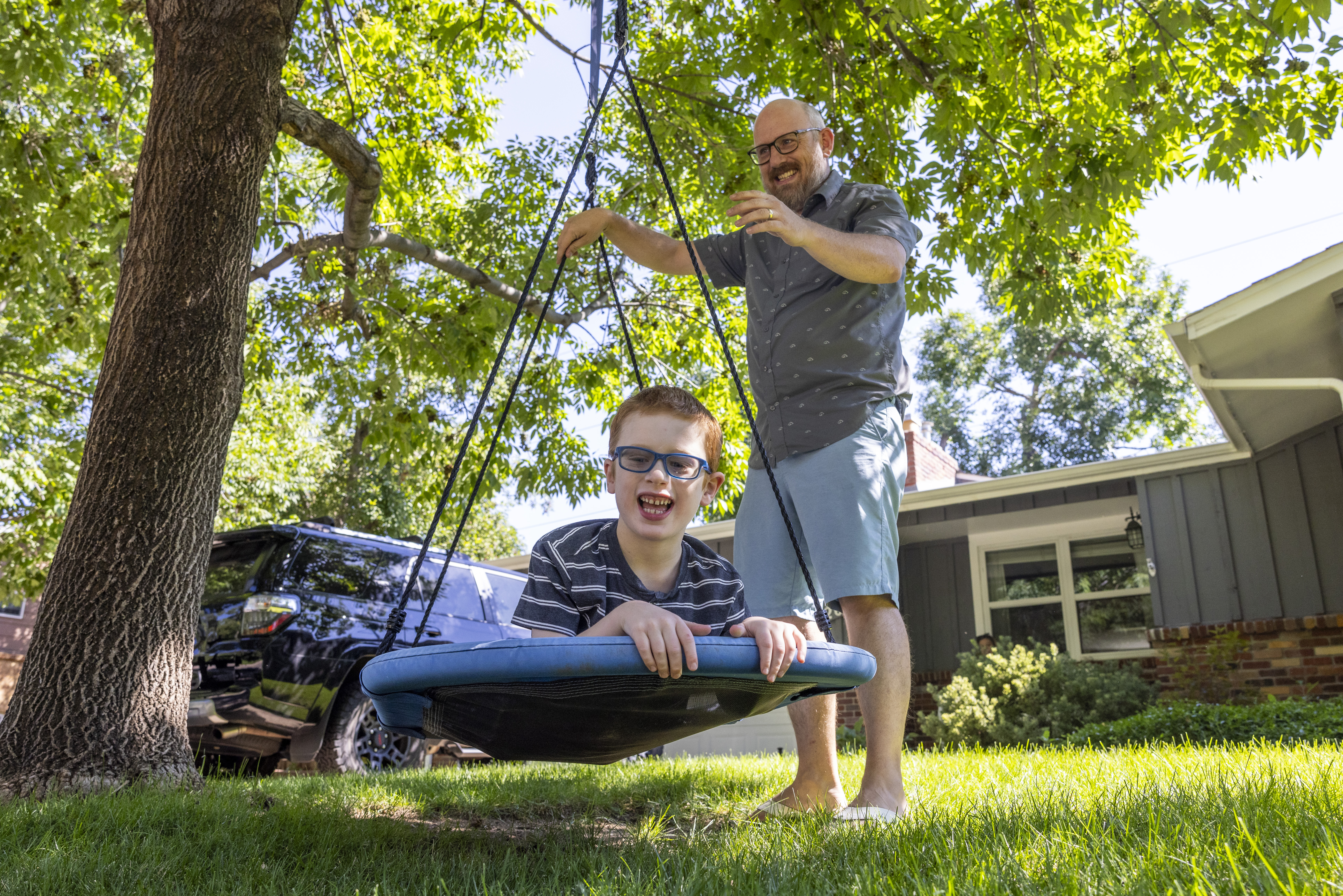 Brian Burkhardt pushes his son Connor on a swing at their home in Centennial on Wednesday, Aug. 9, 2023. Though Connor's diagnosis of the rare genetic disorder Batten disease means his lifespan will be shorter, his bi-weekly medication from Children's Hospital has slowed the progression and allowed him to live a fuller life. (Photo by Grace Smith/The Denver Post)