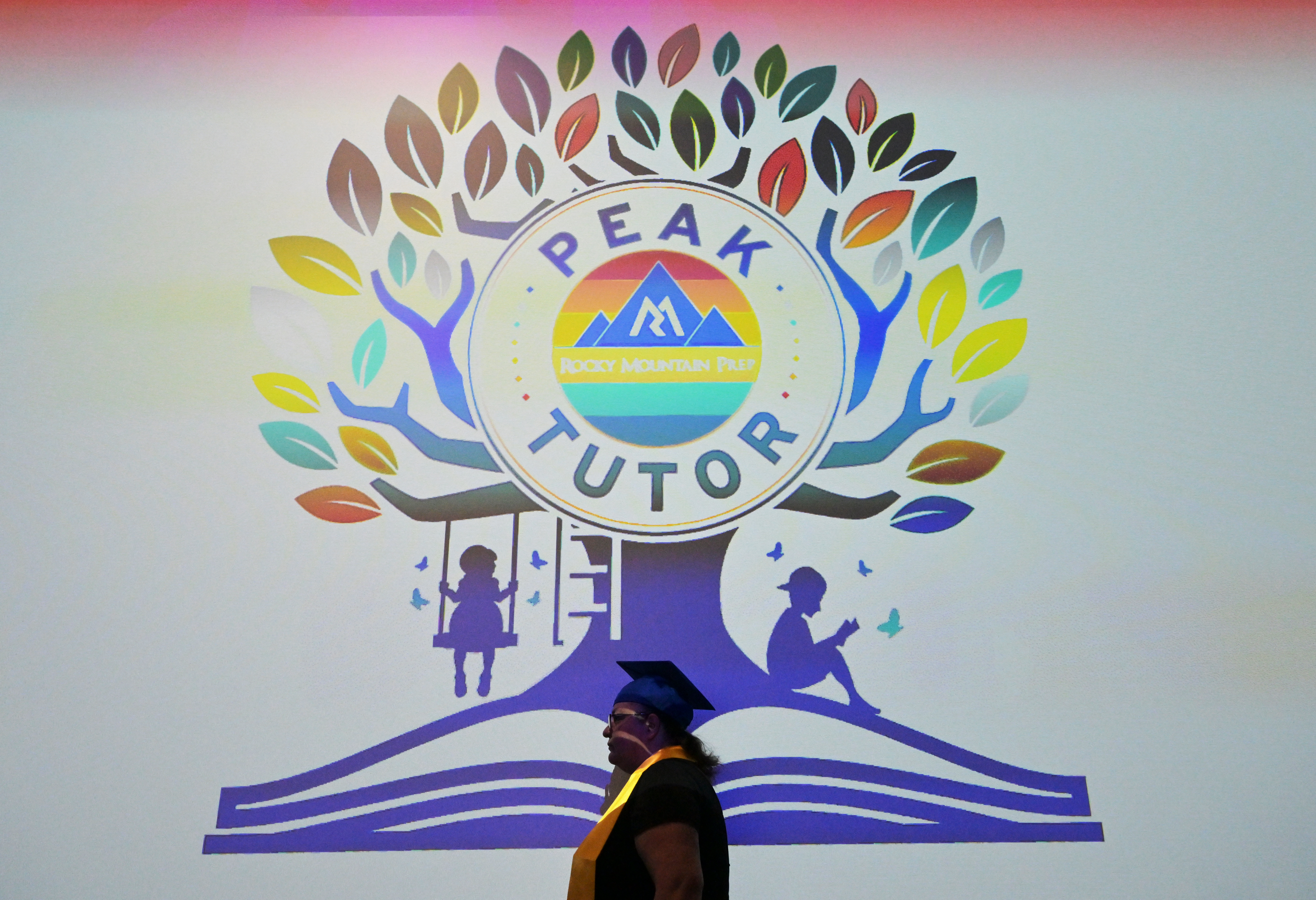 Rosy Maldonado walks past a large screen during a graduation ceremony for the Rocky Mountain Prep's Peak Family Tutor program in Denver on Feb. 10, 2025. The program aims to boost literacy and financial opportunity for the graduates and their families. (Photo by RJ Sangosti/The Denver Post)