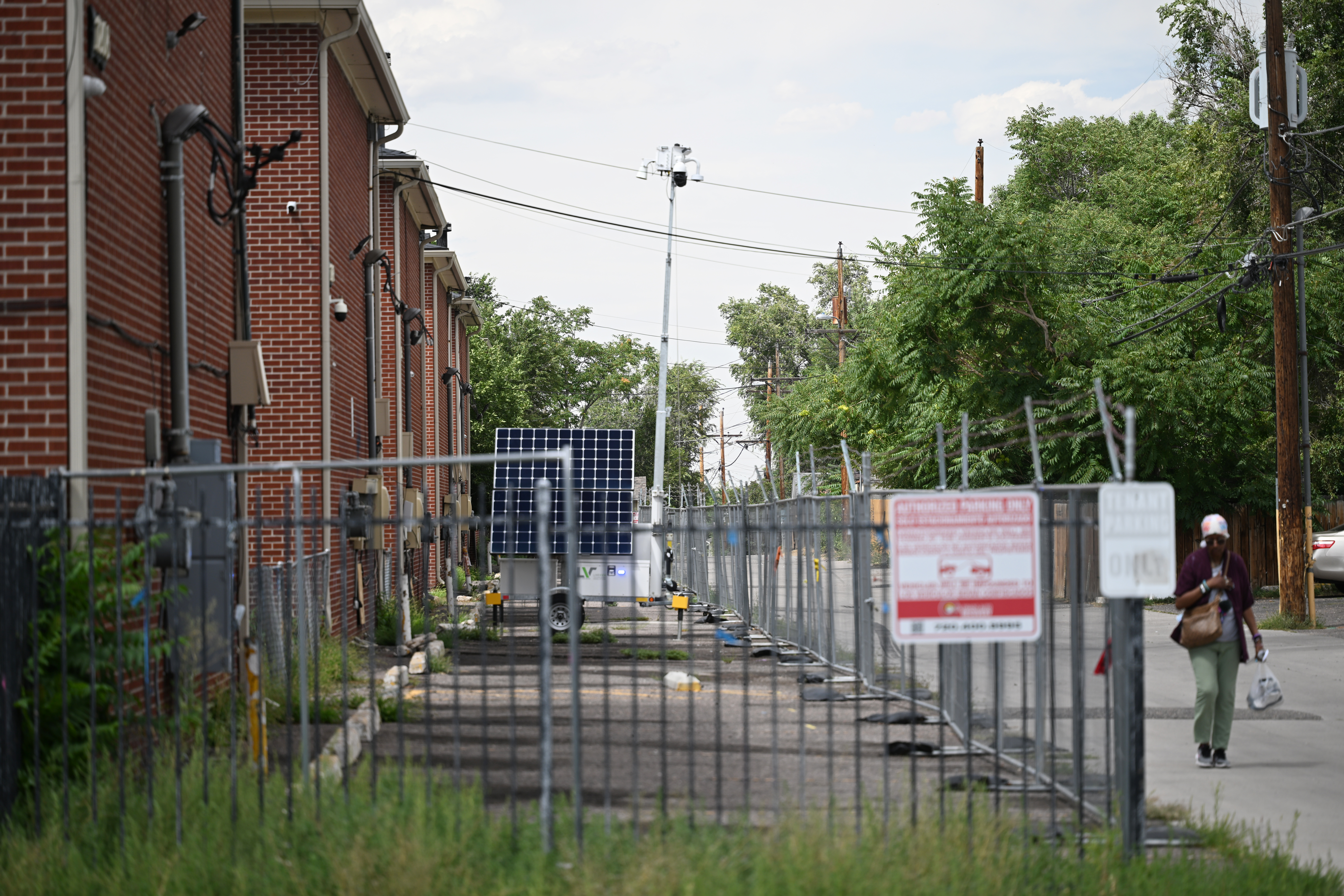 A woman walks down the alley behind the Edge of Lowry property, which is fenced off, with most windows and doors boarded up in Aurora on Aug. 7, 2025. Security devices still monitor the site. (Photo by RJ Sangosti/The Denver Post)